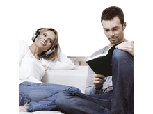 Charger l&#39;image dans la galerie, Une femme avec un casque sourit tandis qu&#39;un homme lit un livre, tous deux sur un canapé blanc.
