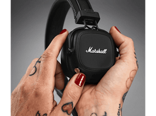 Charger l&#39;image dans la galerie, Mains tatouées tenant un casque Marshall noir, vernis à ongles rouge, bouton doré.
