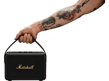 Charger l&#39;image dans la galerie, Un homme tient un haut-parleur noir avec le logo Marshall. Son bras est couvert de tatouages et le fond est blanc.
