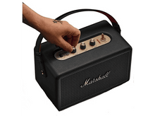 Charger l&#39;image dans la galerie, Un haut-parleur Marshall noir avec une main ajustant un bouton. Le haut-parleur a des accents dorés et une poignée. Le logo Marshall est visible.
