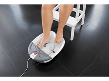 Charger l&#39;image dans la galerie, Pieds d&#39;une personne dans un bain de pieds, eau avec des bulles. Tabouret blanc et sol carrelé noir.
