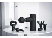 Charger l'image dans la galerie, Pistolet de massage noir avec accessoires sur une table blanche. Fond blanc et serviette derrière.
