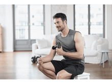 Charger l'image dans la galerie, Homme utilisant un pistolet de massage sur son bras. Il est dans un salon.
