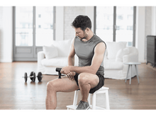 Charger l'image dans la galerie, Homme utilisant un pistolet de massage sur sa cuisse, assis sur un tabouret.
