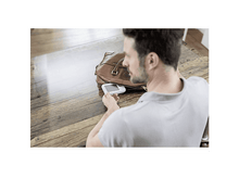 Charger l&#39;image dans la galerie, Un homme regarde un petit appareil dans un sac marron sur une table en bois. L&#39;appareil est blanc.
