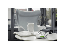 Charger l&#39;image dans la galerie, Un moniteur de tension artérielle et une tasse sur une table. Une chaise est visible en arrière-plan.
