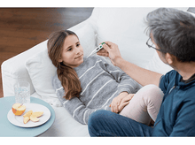 Charger l&#39;image dans la galerie, Une fille allongée sur un canapé prend sa température.
