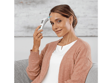 Charger l&#39;image dans la galerie, Une femme prend sa température avec un thermomètre sans contact. Le fond est un mur blanc.
