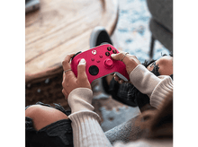 Charger l&#39;image dans la galerie, Une personne tient une manette Xbox rose. La personne porte un pull beige et un jean.
