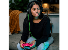 Charger l&#39;image dans la galerie, Une femme portant un casque joue sur un canapé, tenant une manette rose.
