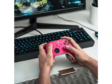 Charger l&#39;image dans la galerie, Mains tenant une manette Xbox rose au-dessus d&#39;un clavier et d&#39;un moniteur.
