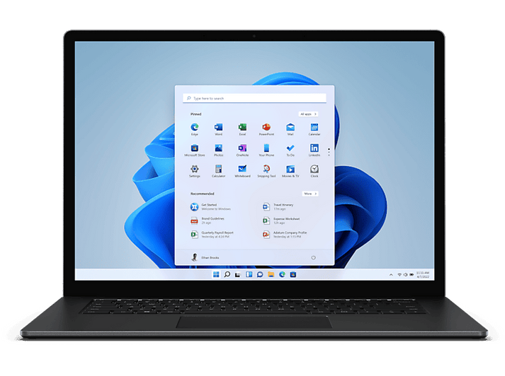Un ordinateur portable affiche le menu Démarrer de Windows 11. Des icônes d'applications et une barre de recherche sont visibles sur un fond abstrait bleu et blanc.