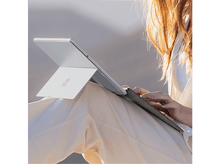 Charger l&#39;image dans la galerie, Femme utilisant une tablette argentée avec un pantalon blanc dans un cadre naturel, avec soleil et arrière-plan flou.
