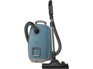 Aspirateur Miele bleu avec des accents argentés, un tuyau et une brosse. Fond noir.