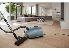 Charger l&#39;image dans la galerie, Un aspirateur bleu sur un sol en bois, tuyau et tête visibles. Intérieur lumineux et propre.
