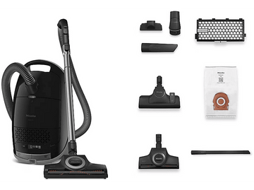 Un aspirateur noir avec accessoires, dont des brosses, et un sac à poussière sur une surface blanche.