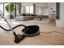 Charger l&#39;image dans la galerie, Un aspirateur noir et gris sur un plancher en bois, avec une fenêtre en arrière-plan.
