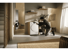 Charger l&#39;image dans la galerie, Un homme à genoux dans une pièce moderne, interagissant avec une machine à laver.
