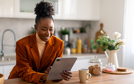 Une jeune femme se sert d'une tablette accoudée sur le plan de travail d'une cuisine.