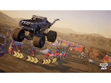 Charger l&#39;image dans la galerie, Un monster truck sautant par-dessus des obstacles, dans un environnement désertique, avec un coucher de soleil.
