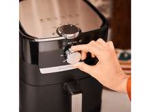 Charger l&#39;image dans la galerie, Une main tourne un cadran sur une friteuse à air noire avec un dessus en acier inoxydable.
