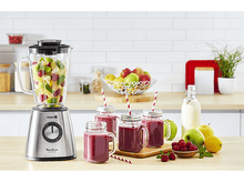 Charger l&#39;image dans la galerie, Un mixeur avec des fruits et des smoothies dans des bocaux sur une planche en bois. Des pailles et des fruits sont présents.
