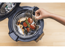 Charger l&#39;image dans la galerie, Une main plaçant un sac de légumes dans une cocotte-minute. La cocotte est noire avec un intérieur argenté.
