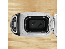 Charger l&#39;image dans la galerie, Machine à pain, vue de dessus. Ouverte, montrant l&#39;intérieur, avec la cuve et les pales. Commandes à gauche.
