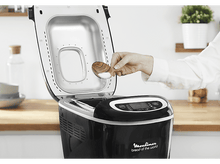 Charger l&#39;image dans la galerie, Une personne ajoute du sel à une machine à pain. La machine à pain est noire et possède un affichage numérique.

