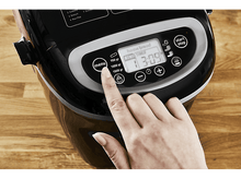 Charger l&#39;image dans la galerie, Une main appuie sur le bouton menu d&#39;une machine à pain noire. L&#39;écran affiche la minuterie et les paramètres.
