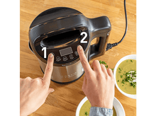 Charger l&#39;image dans la galerie, Mains appuyant sur les boutons d&#39;un robot culinaire noir et argenté, avec des bols de soupe.
