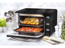 Charger l&#39;image dans la galerie, Four noir avec nourriture à l&#39;intérieur, porte ouverte et ustensiles sur le côté.
