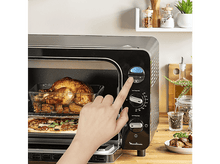 Charger l&#39;image dans la galerie, La main d&#39;une personne réglant la minuterie sur un four Moulinex noir avec de la nourriture à l&#39;intérieur. Surface en bois.
