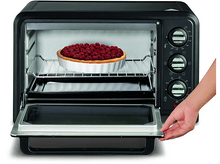 Charger l&#39;image dans la galerie, Un four grille-pain noir avec la porte ouverte et une tarte à l&#39;intérieur, une main à droite.
