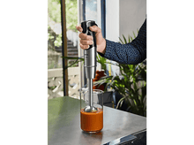 Charger l&#39;image dans la galerie, Personne mixant de la soupe avec un mixeur plongeant Tefal dans un verre. Soupe orange visible.
