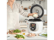 Charger l&#39;image dans la galerie, Une personne ajoutant des oignons dans une cocotte Moulinex avec des ingrédients autour.
