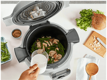 Charger l&#39;image dans la galerie, Un autocuiseur ouvert avec des ingrédients et une main tenant un verre de liquide.
