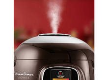 Charger l&#39;image dans la galerie, Un autocuiseur marron et argenté avec de la vapeur ascendante, fond rouge.
