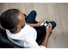 Charger l&#39;image dans la galerie, Homme assis dans une chaise, tenant une manette de jeu blanche, jouant à un jeu.
