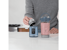 Charger l&#39;image dans la galerie, Personne versant d&#39;un couvercle gris dans une base de mixeur bleue. Smoothie rose à l&#39;intérieur.
