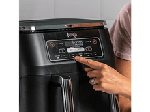 Charger l'image dans la galerie, Friteuse à air Ninja noire. Main appuyant sur un bouton. Fond noir.
