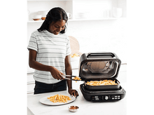 Charger l&#39;image dans la galerie, Femme plaçant des frites dans une assiette. Friteuse à air et frites sur le comptoir.
