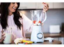 Charger l&#39;image dans la galerie, Femme ajoutant une fraise dans un blender avec des fruits et un pot de lait.

