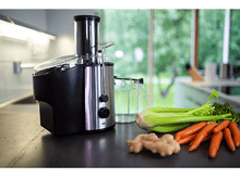 Charger l&#39;image dans la galerie, Un extracteur de jus avec des légumes comme des carottes, du céleri et du gingembre sur un comptoir noir.
