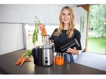 Charger l&#39;image dans la galerie, Femme tenant des carottes et un presse-agrumes. Le jus est dans un verre.
