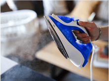 Charger l&#39;image dans la galerie, Fer à repasser bleu et blanc, vapeur visible, tenu à la main. Arrière-plan flou.
