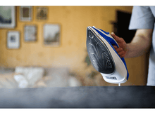 Charger l&#39;image dans la galerie, Fer à repasser avec vapeur sur une surface noire. Personne tenant le fer en arrière-plan.

