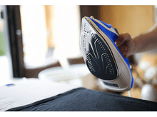 Charger l&#39;image dans la galerie, Fer à repasser en cours d&#39;utilisation. Une main tient le fer sur un tissu noir.
