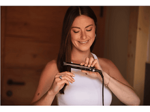 Charger l&#39;image dans la galerie, Une femme utilise un lisseur, souriante, dans une pièce bien éclairée.
