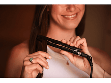 Charger l&#39;image dans la galerie, Femme utilisant un lisseur noir, souriante, avec une bague, sur fond flou.
